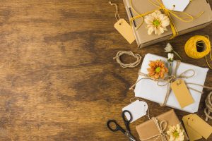 Wrapped gift with empty tag and beautiful flower over wooden table